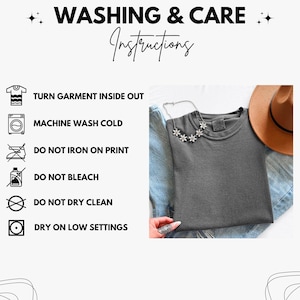 May include: A dark grey t-shirt with a daisy necklace and a brown hat. The image includes washing instructions: Turn garment inside out, machine wash cold, do not iron on print, do not bleach, do not dry clean, and dry on low settings.