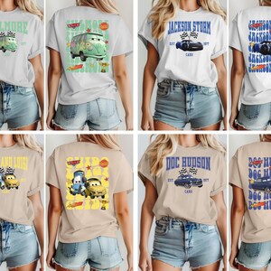 May include: Collection of t-shirts featuring various car-themed designs. The shirts display images of cartoon cars and text such as "VILLMORE", "JACKSON STORM", and "DOC HUDSON". The shirts are in various colors, including white and tan.