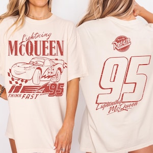May include: A cream-coloured t-shirt with a red graphic of Lightning McQueen race car and the text "Lightning McQueen" and "95". The back of the shirt has a large "95" and "Lightning McQueen" in red.
