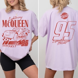 May include: Pale purple t-shirt with a red Lightning McQueen design. The front shows the car, text, and the number 95. The back of the shirt has the number 95 and the text "Lightning McQueen".