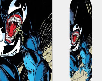 May include: A skateboard deck featuring a comic book illustration of Venom. The design showcases Venom's white eyes, sharp teeth, and red mouth against a black and blue background. The board has a curved shape.