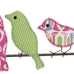 May include: Three colorful fabric birds perched on a brown branch. The birds are pink, green, and pink and white with a geometric pattern. The birds are all facing the right side of the image.
