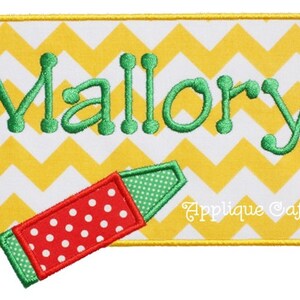 Puede incluir: Un rectángulo de tela con estampado de chevron amarillo y blanco con el nombre "Mallory" bordado en verde. Un crayón rojo y verde con lunares blancos está sobre el rectángulo. El texto "Applique Cafe" está en blanco en la parte inferior del rectángulo.