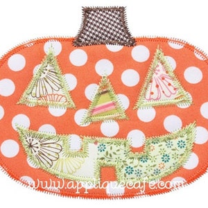 Puede incluir: Un aplique con forma de calabaza naranja con lunares blancos y un contorno cosido. La calabaza tiene ojos triangulares y una boca dentada, todos rellenos de tela estampada. El tallo es de tela de pata de gallo marrón y blanca. El sitio web www.appliquecafe.com es visible.