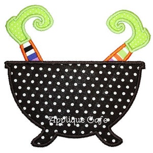 May include: Black cauldron with white polka dots and two green and orange witch's broomsticks sticking out of the top. "Applique Cafe" is written in white on the front of the cauldron.