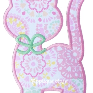 May include: Pink and green applique cat with a bow. The cat is made of fabric with a floral pattern and has a pink outline.