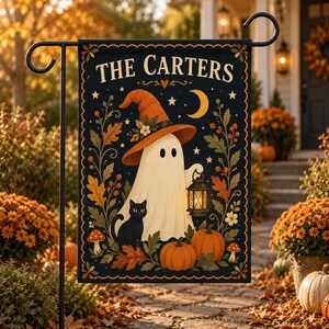 May include: A rectangular garden flag featuring a black background with the text THE CARTERS at the top. A white ghost wearing an orange witch hat holds a lit lantern, accompanied by a black cat, pumpkins, mushrooms, and autumn leaves.