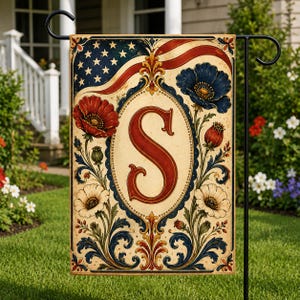 May include: A garden flag with an American flag design in red, white, and blue. The flag has a large red letter "S" in an oval frame, surrounded by floral elements. The flag is displayed on a black metal stand, suitable for a garden.
