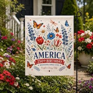 Könnte beinhalten: Eine rechteckige Gartenflagge mit cremefarbenem Hintergrund, verziert mit einem Blumenarrangement aus blauen, roten und weißen Blüten, Schmetterlingen und Libellen. Der Text lautet: AMERICA 250TH BIRTHDAY RESISTING SINCE 1776 Foxglove Daisy Tulip.