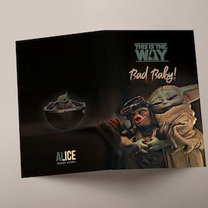 Può includere: Biglietto di auguri piegato con sfondo scuro. Il fronte presenta il testo "THIS IS THE WAY" e "Bad Baby!" con l'immagine di un personaggio che abbraccia Grogu. L'interno mostra Grogu in una capsula fluttuante.