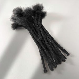 Può includere: Un fascio di extension per capelli neri caratterizzato da un aspetto testurizzato e arrotolato. Ogni singola ciocca presenta una struttura spessa e opaca con estremità sciolte e crespe sulla parte superiore, creando un'estetica scura uniforme.