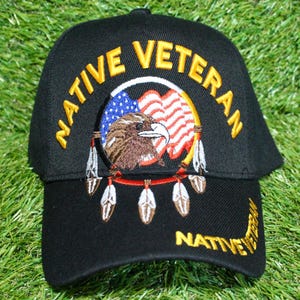 May include: Black baseball cap with embroidered text "NATIVE VETERAN" in gold. The cap features an emblem with an eagle, American flag, and feathers. The brim also has the word "NATIVE" in gold.