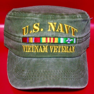 Può includere: Berretto in stile militare verde oliva con la scritta "U.S. NAVY" e "VIETNAM VETERAN" ricamata in oro. Sopra il testo è cucita una barra di nastro colorata. Il berretto ha una visiera curva e una corona strutturata.