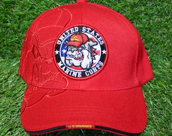 May include: A red baseball cap featuring the United States Marine Corps emblem. The emblem is a circular patch with a bulldog wearing a helmet. The cap has a curved brim and a textured design on the side.