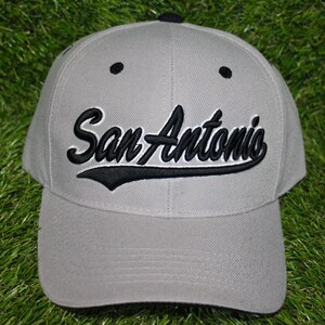 May include: A gray baseball cap with black embroidery that reads "San Antonio".