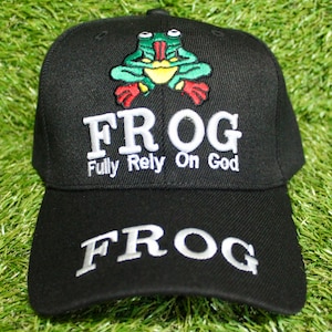 May include: A black baseball cap featuring an embroidered green, red, and yellow frog graphic at the top. Below the frog, the word FROG is embroidered in white, followed by the text Fully Rely On God. The word FROG is also embroidered on the brim.