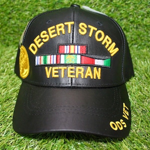 Puede incluir: Gorra de béisbol de cuero negro con texto bordado en amarillo "Desert Storm Veteran" y un parche bordado en oro. La gorra tiene un "ODS VET" bordado en amarillo en el lateral.