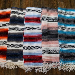 May include: A collection of colorful woven blankets with fringed edges. The blankets feature horizontal stripes in various colors, including orange, blue, red, pink, and turquoise, with a repeating geometric pattern in black and white.