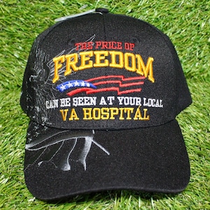 May include: Black baseball cap with embroidered text "THE PRICE OF FREEDOM" in yellow and red, with a flag design. The text "CAN BE SEEN AT YOUR LOCAL VA HOSPITAL" is also embroidered on the cap. Features an eagle design on the side.
