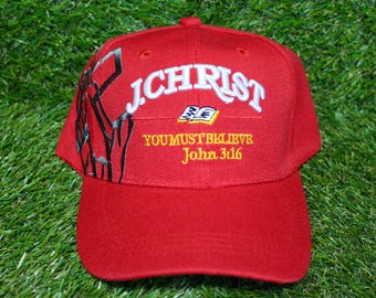 May include: Red baseball cap with the words "I CHRIST YOU MUST BELIEVE John 3:16" embroidered on the front. The cap has a black and white image of a person praying on the side.