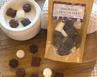 Puede incluir: Una bolsa de chocolates surtidos con el texto "Griffin Oaks Assorted Chocolates" y "Scented Wax Melts Hand Poured in Clermont, FL. Soy Wax Blend. 3 oz (85g) Net Weight". Los chocolates están en una bolsa transparente con un respaldo de papel marrón. Los chocolates son de varias formas y tamaños, incluyendo cuadrados, círculos y rectángulos. Algunos de los chocolates son blancos, mientras que otros son marrones.