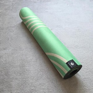 May include: A rolled up green yoga mat with white stripes and a black label that says "Namast&eacute; Yogi".