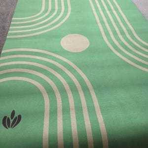 May include: Green yoga mat with a pattern of tan concentric circles and a tan circle in the center. The mat has a small, dark green logo in the lower left corner.