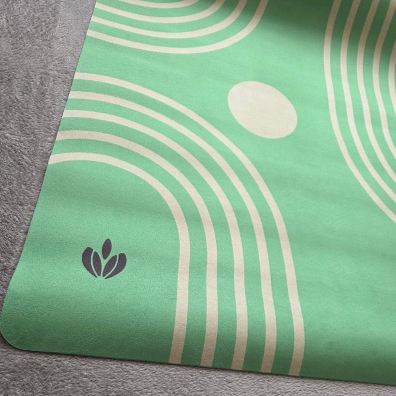 May include: A green yoga mat with a white and cream geometric pattern. The mat has a small, dark green logo in the lower left corner.