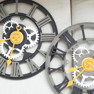 May include: Two black and white clock faces with Roman numeral markings and intricate gear designs. The gears are layered and have a yellow accent.