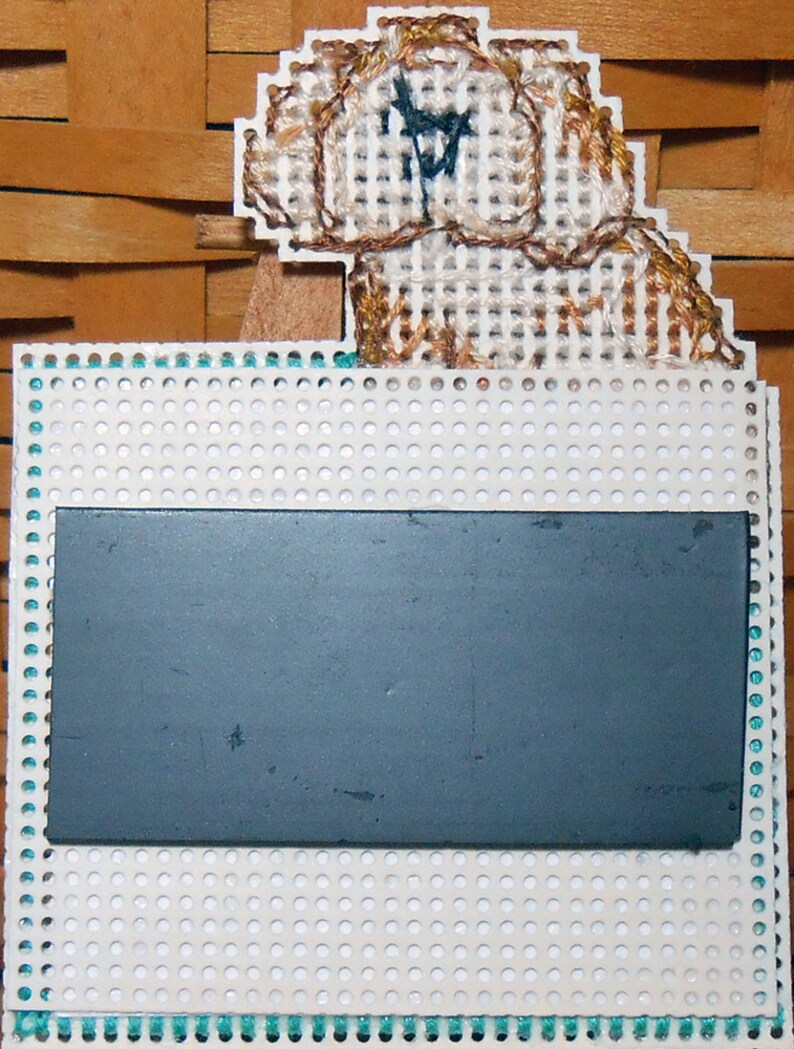 A photo of the back of the magnet. The square portion has a second layer of perforated paper attached with a piece of card stock sandwiched in between. The magnet itself covers the middle of the square portion. The dog is unlined.