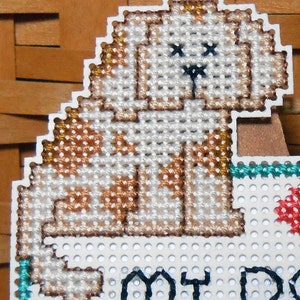 A close up of the dog stitched in the upper left corner. He is a light brown color with darker brown spots and black eyes and nose.