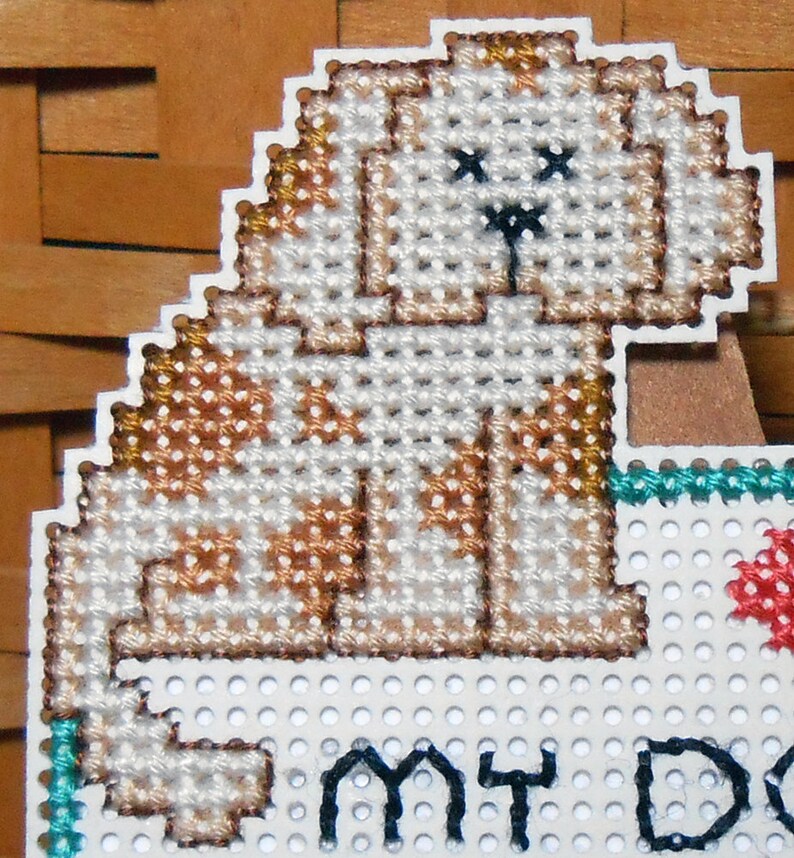 A close up of the dog stitched in the upper left corner. He is a light brown color with darker brown spots and black eyes and nose.