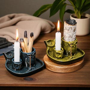 May include: Two ceramic incense holders, one teal and one olive green, each with a candle and a place for incense sticks. The teal holder has a lit candle and a bundle of incense sticks. The olive green holder has a lit candle and a bundle of sage.