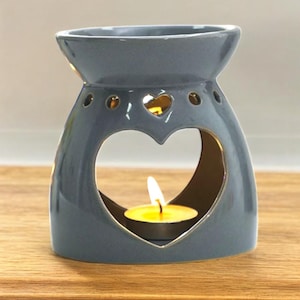May include: A gray ceramic oil diffuser with a heart-shaped opening and a small tea light candle inside. The diffuser has a decorative gold trim around the heart opening.