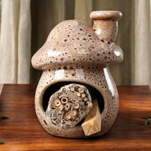 Puede incluir: Un portaincienso de cerámica con forma de hongo en marrón y beige moteado. El soporte tiene una chimenea y una gran abertura para sostener palitos de incienso y un trozo de madera. El soporte está sobre una superficie de madera.