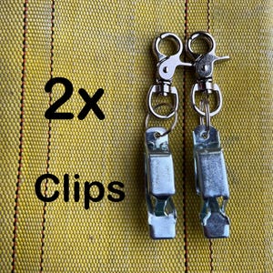 May include: Two silver metal clips with a silver swivel hook and a silver ring. The text "2x Clips" is visible in the image.