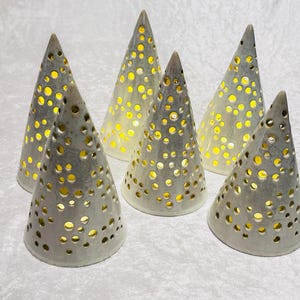 Puede incluir: Seis candelabros cónicos de cerámica con numerosas aberturas circulares. Los soportes son de color gris claro y el interior brilla con una cálida luz amarilla. Estas piezas decorativas son ideales para la decoración del hogar.