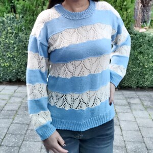 May include: A blue and white striped sweater with a crocheted design. The sweater has long sleeves and a round neckline.