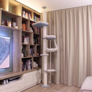 Op de afbeelding: Een moderne krabpaal met meerdere niveaus, inclusief een bovenste ligplaats, een hangmat en platforms. De krabpaal is wit met lichtblauwe accenten en biedt katten een comfortabele en stimulerende ruimte.