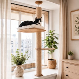 May include: A floor-to-ceiling cat tree featuring a central vertical post wrapped in natural sisal rope, a square wooden platform with a soft white cushion, and a smaller secondary wooden shelf, all designed for feline climbing and resting.