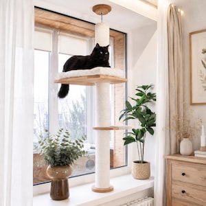 May include: A floor-to-ceiling cat tree featuring a central vertical post wrapped in light-colored sisal rope, two wooden platforms, and a soft white cushion. A long-haired black cat is resting on the top platform near a window.
