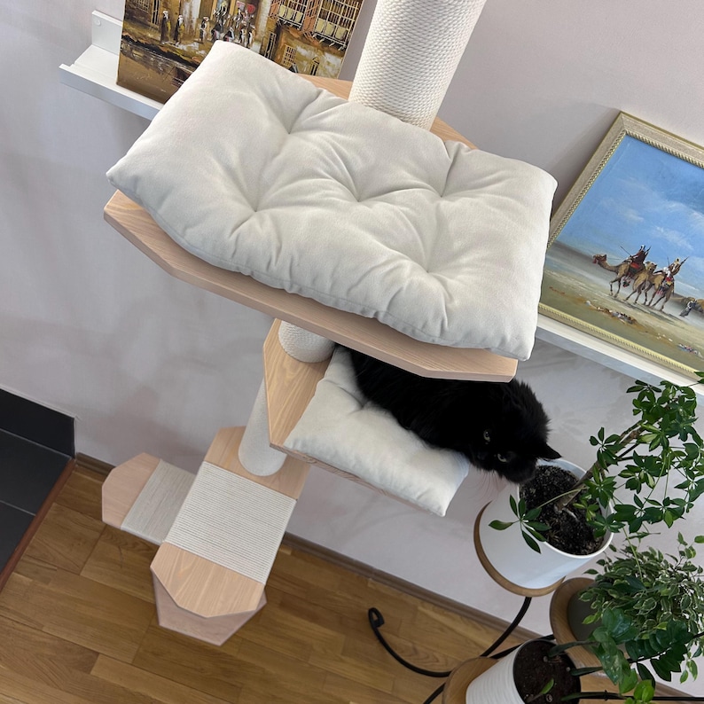 May include: A white cat tree with multiple platforms and a scratching post. The top platform has a white cushion. A black cat is lying on a lower platform with a white cushion.