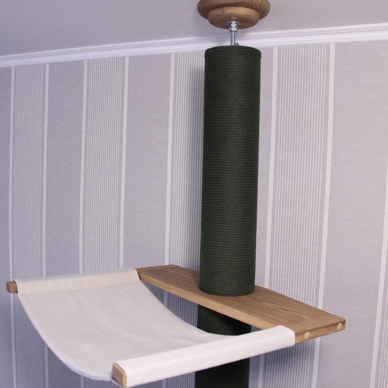 May include: A cat tree with a dark green scratching post, a wooden platform, and a white hammock. The tree is mounted to the ceiling with a wooden base. The background is a striped wallpaper.