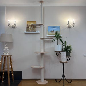 May include: A tall, beige cat tree with multiple platforms and a scratching post. The tree is made of wood and sisal rope, with a hexagonal base and a ceiling-mounted design. The platforms are round and provide a place for cats to climb and rest.