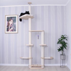 May include: A multi-level cat tree with a black cat resting on the top platform. The cat tree features multiple platforms, scratching posts, and a hanging toy. The structure is made of light-colored wood and beige fabric, set against a striped wall.