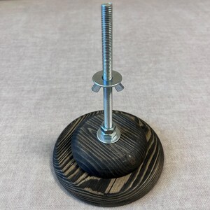 May include: A wooden base with a metal screw and a washer. The base is dark brown with a wood grain pattern.