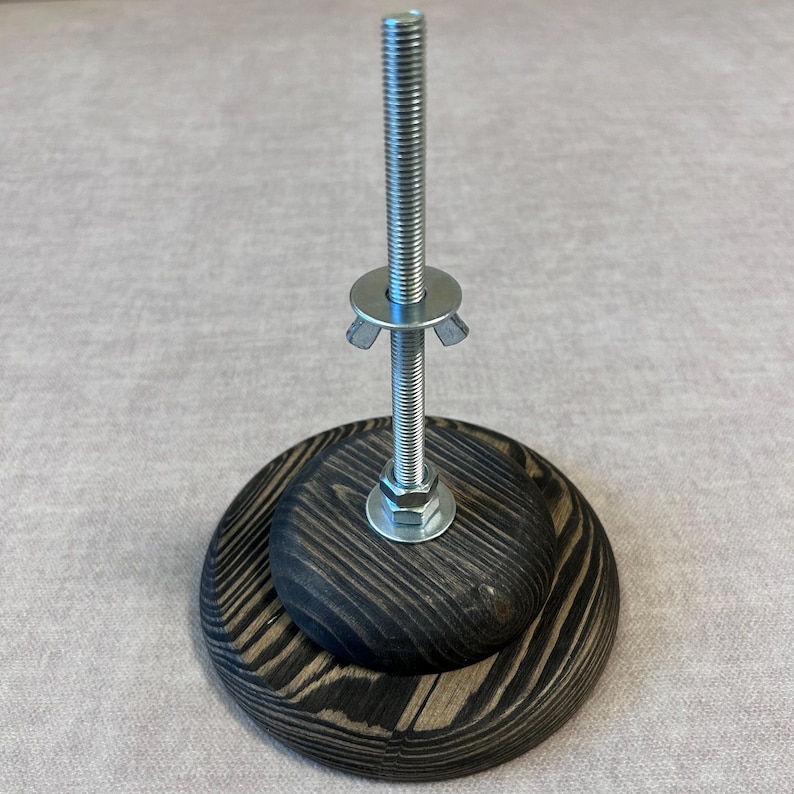 May include: A wooden base with a metal screw and a washer. The base is dark brown with a wood grain pattern.