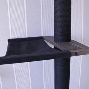 May include: A black cat tree with a dark wooden shelf and a black fabric hammock. The posts are wrapped in black rope. The background is a striped wallpaper.