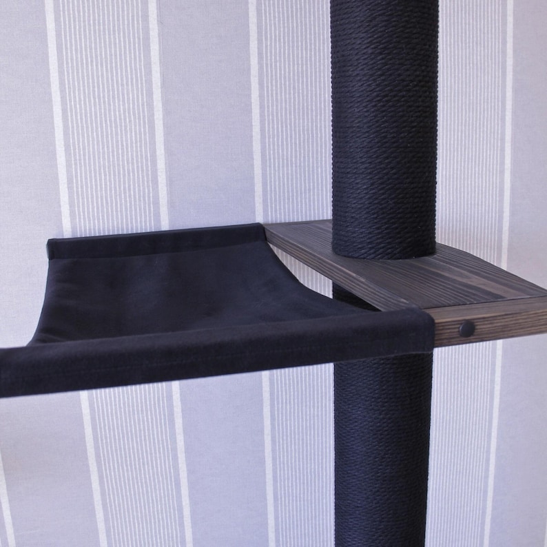 May include: A black cat tree with a dark wooden shelf and a black fabric hammock. The posts are wrapped in black rope. The background is a striped wallpaper.