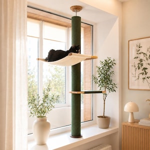 Pode incluir: Uma árvore para gatos do chão ao teto com um poste arranhador alto coberto de sisal verde escuro, uma rede de tecido creme que sustenta um gato preto e uma plataforma de madeira menor com superfície de tecido verde no poste central.